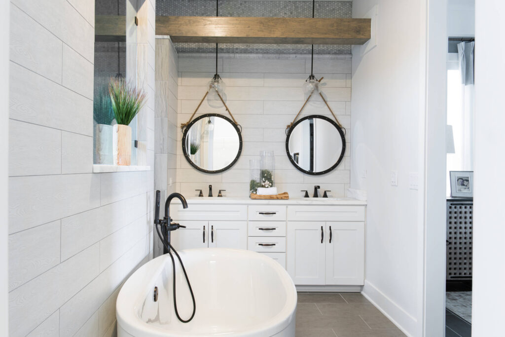 Modern bathroom featuring a freestanding white bathtub with matte black fixtures, double vanity with white cabinets, and two round mirrors suspended by ropes under pendant lights.