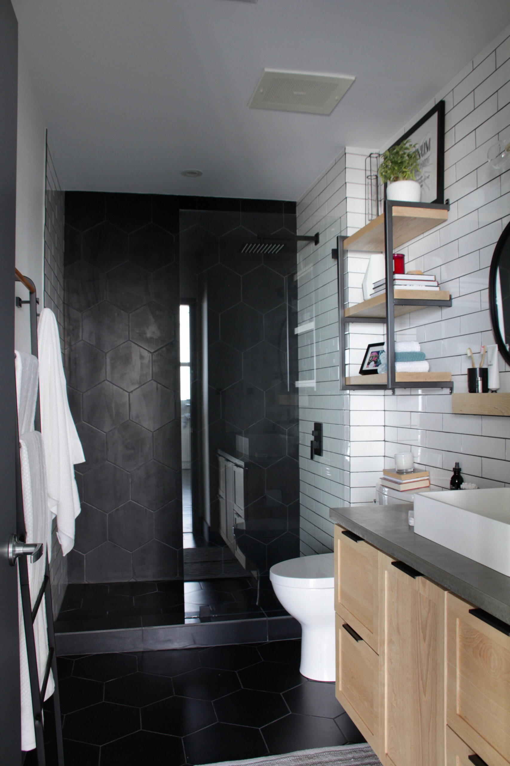 Modern bathroom with black hexagon tiles, wood vanity, and white subway tile walls.