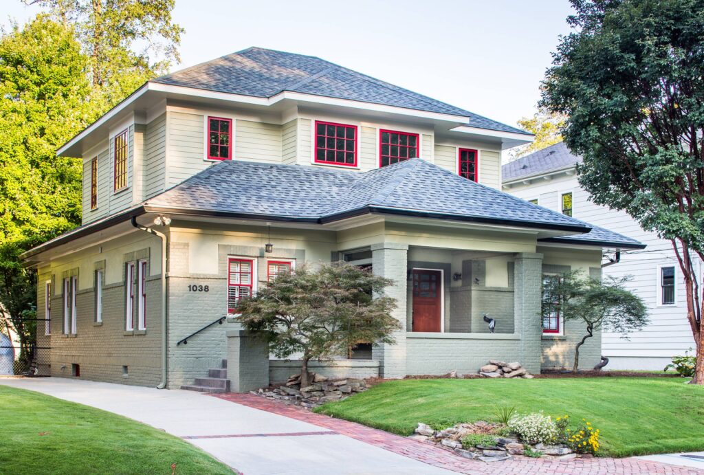 Two-story house with green exterior, red-trimmed windows, and covered front porch.