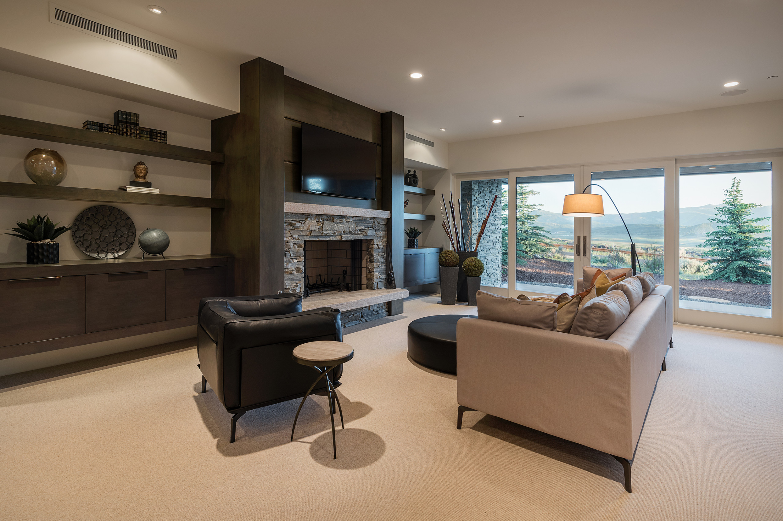 Modern living room with stone fireplace, large windows, and neutral-toned furniture