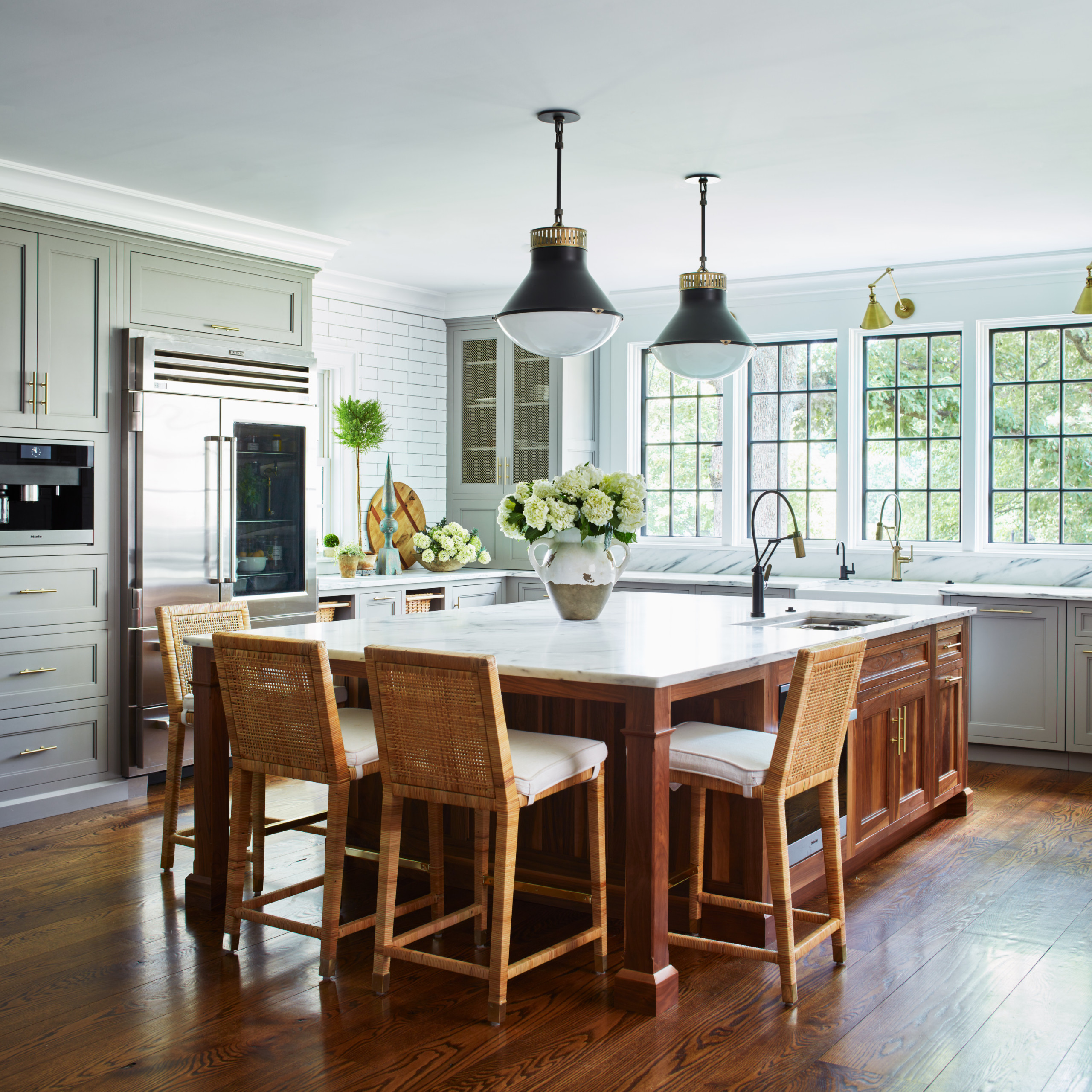 Traditional kitchen with white marble island, wooden base, wicker bar stools, and stainless steel appliances.