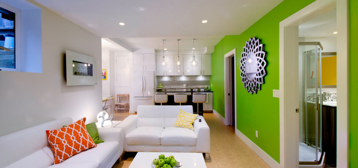 Colorful basement apartment with white furniture, green accent wall, and modern kitchenette.