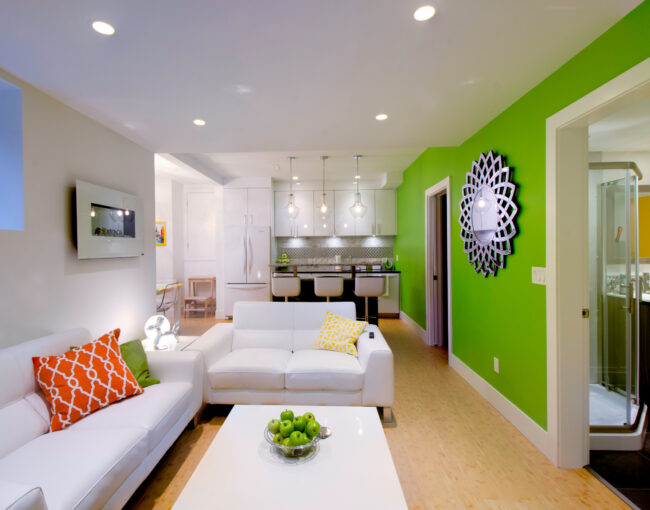 Colorful basement apartment with white furniture, green accent wall, and modern kitchenette.