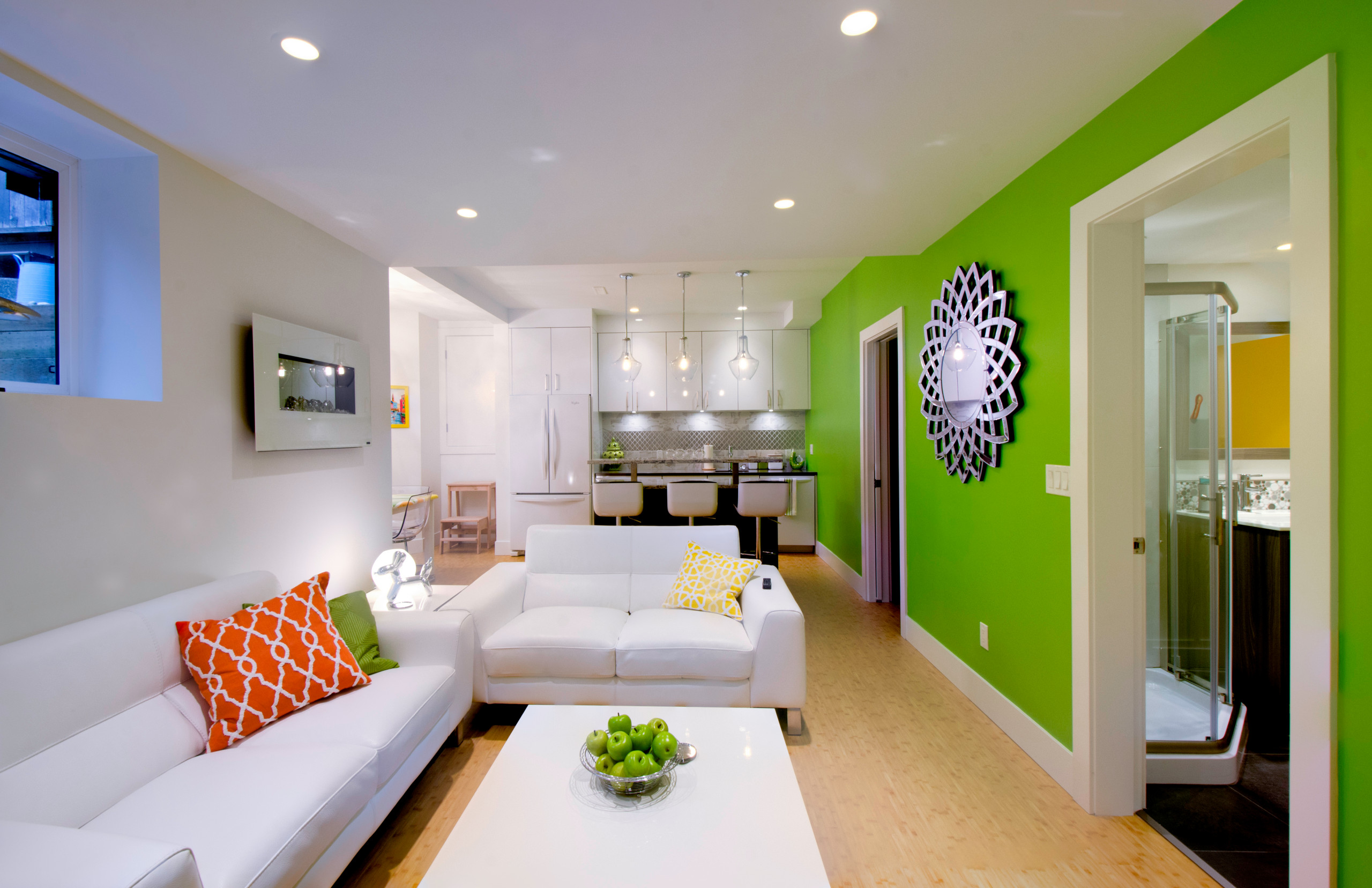 Colorful basement apartment with white furniture, green accent wall, and modern kitchenette.