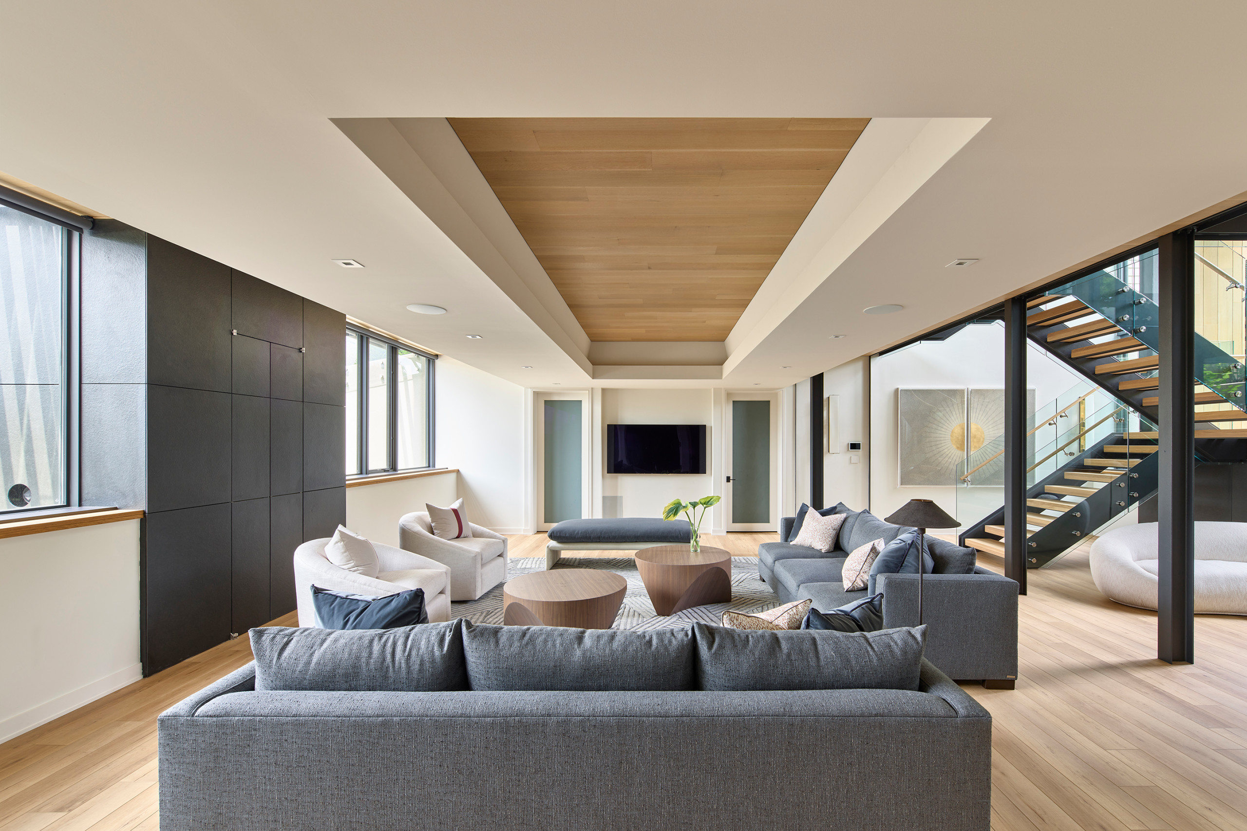 Modern living room with gray sofas, wood accents, and open staircase design.